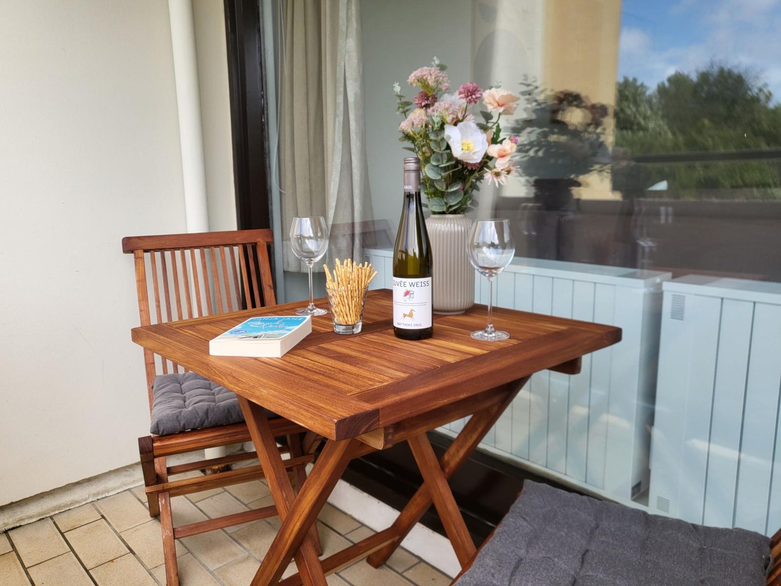 Holztisch mit Stuhl, Weinflasche, Gläsern und Blumen auf Balkon.