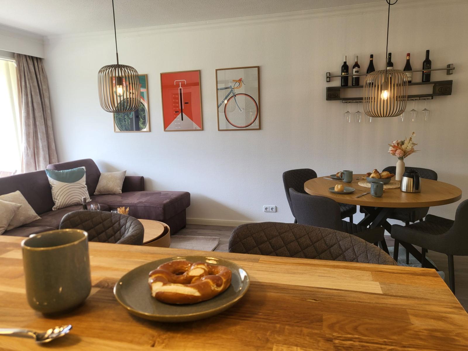 Esszimmer mit runden Tisch, Stühlen und Wandregal mit Weinflaschen.