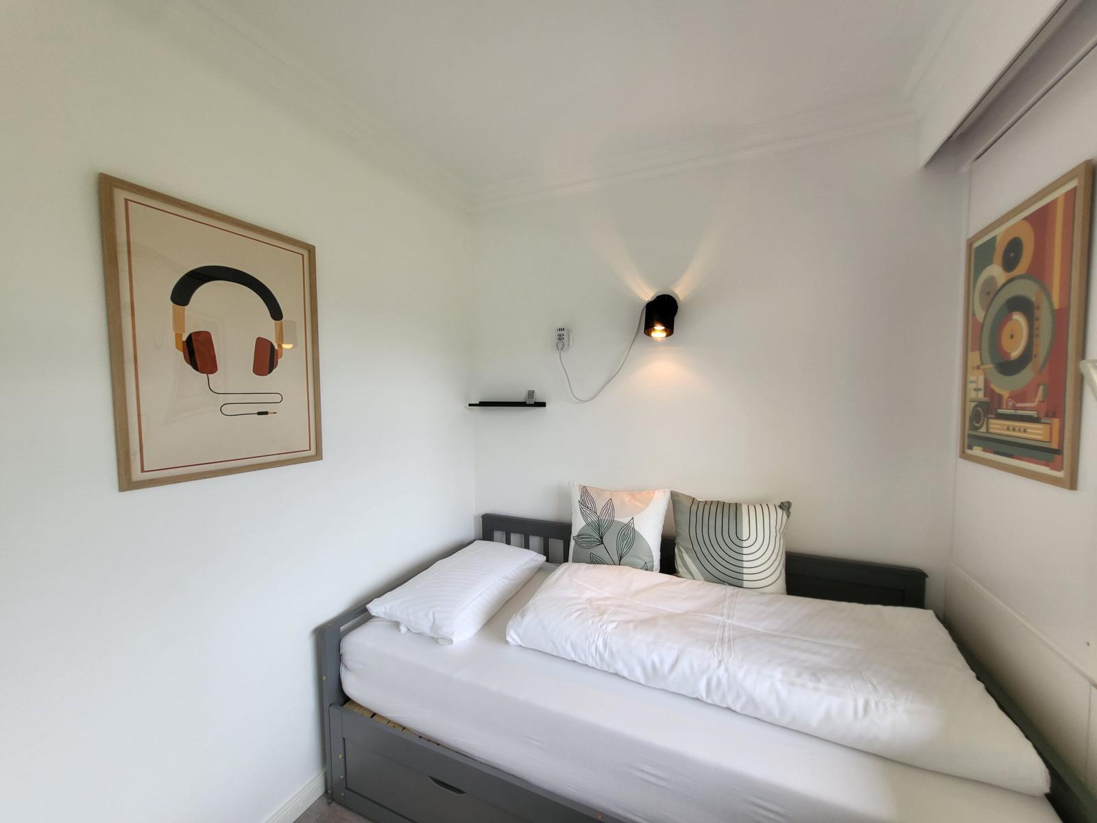 Schlafzimmer mit Bett, Wandbildern und Wandlampe.