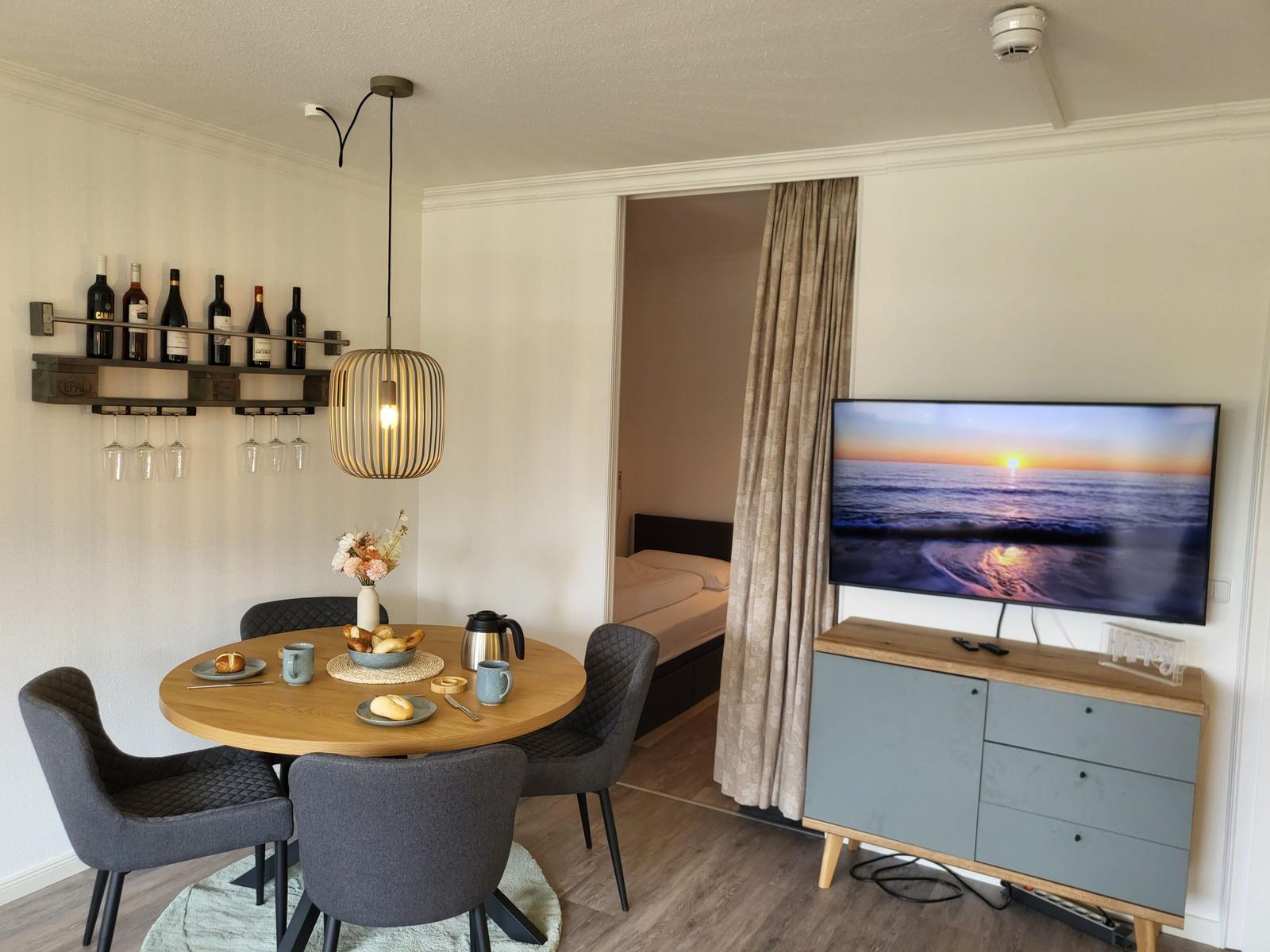 Essbereich mit runden Tisch, vier Stühlen und Fernseher an der Wand.