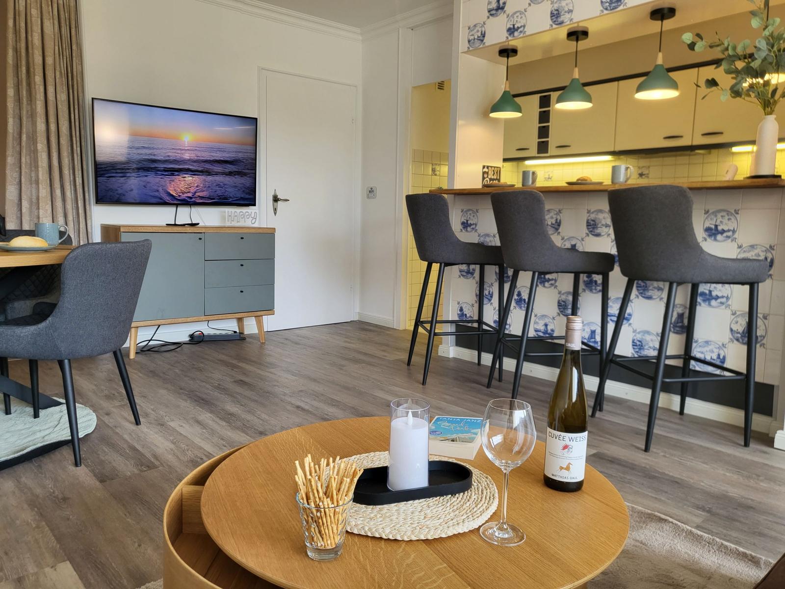 Wohnbereich mit TV, Essbereich und Küchenzeile mit Barhockern.