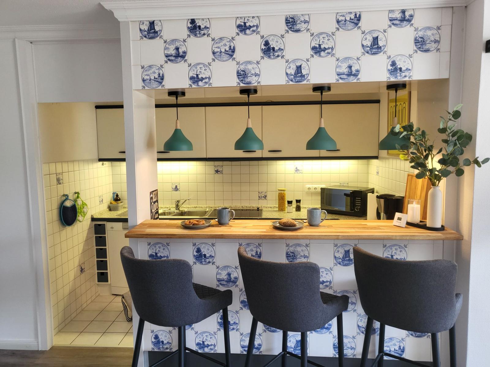 Küche mit Holzbar, drei Stühlen und Delftziegeln an Wand und Bar.