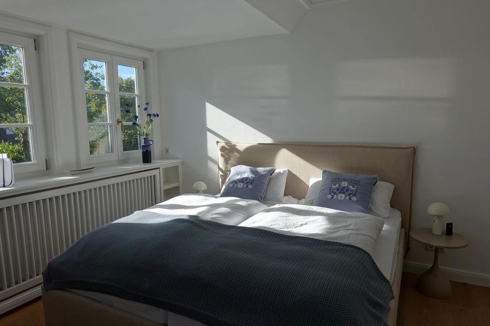 Schlafzimmer mit Doppelbett, Fenstern und Nachttisch.