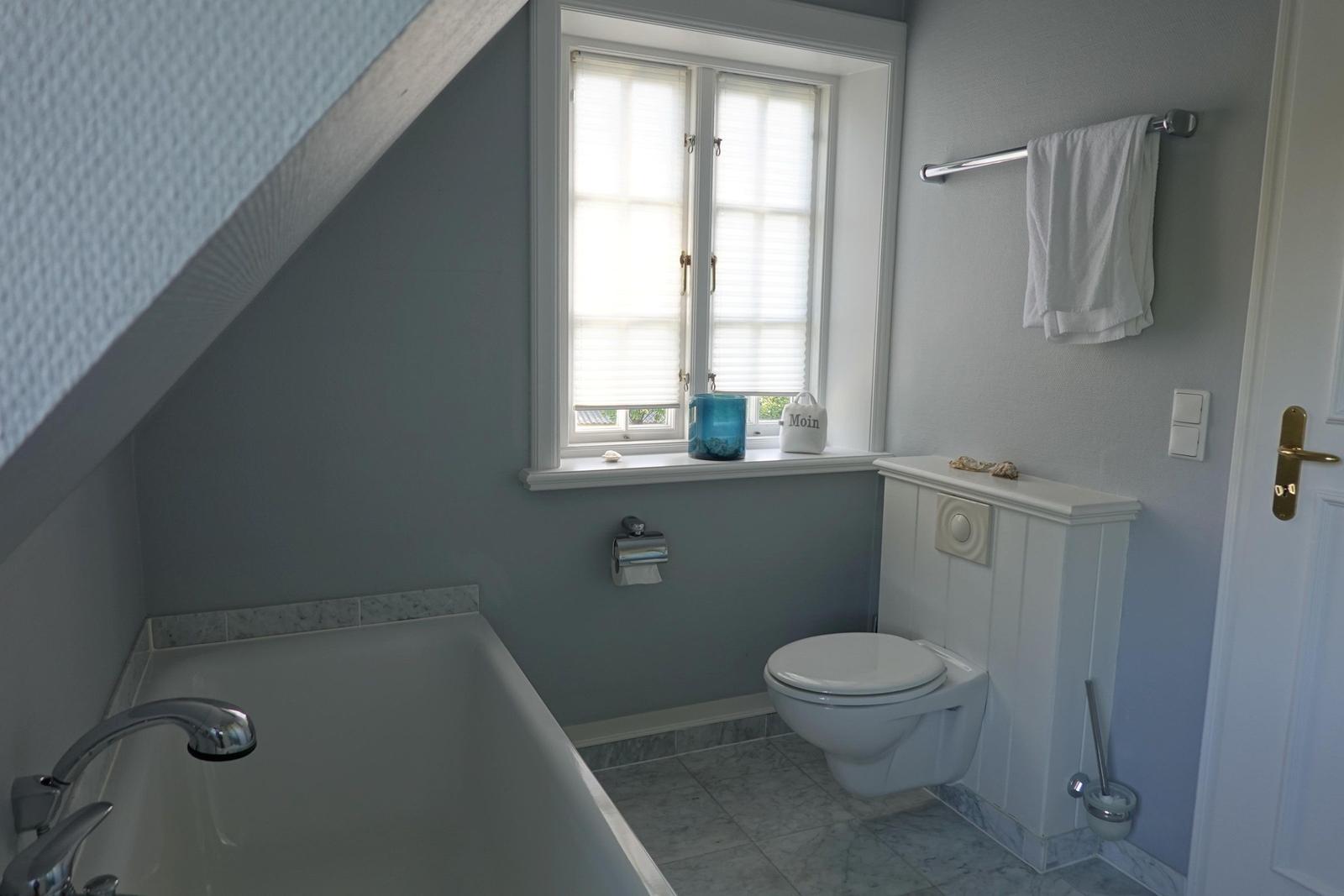 Badezimmer mit Badewanne, Toilette und Fenster mit Jalousie.