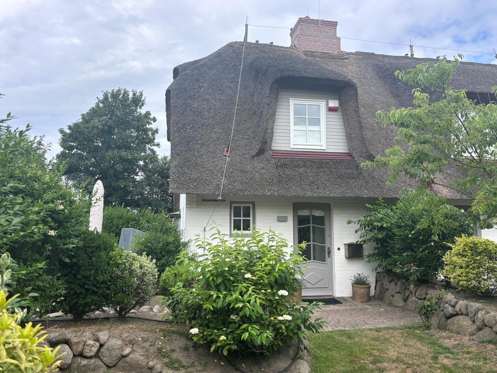 Haus mit Strohdach, weißer Fassade und grüner Umgebung.