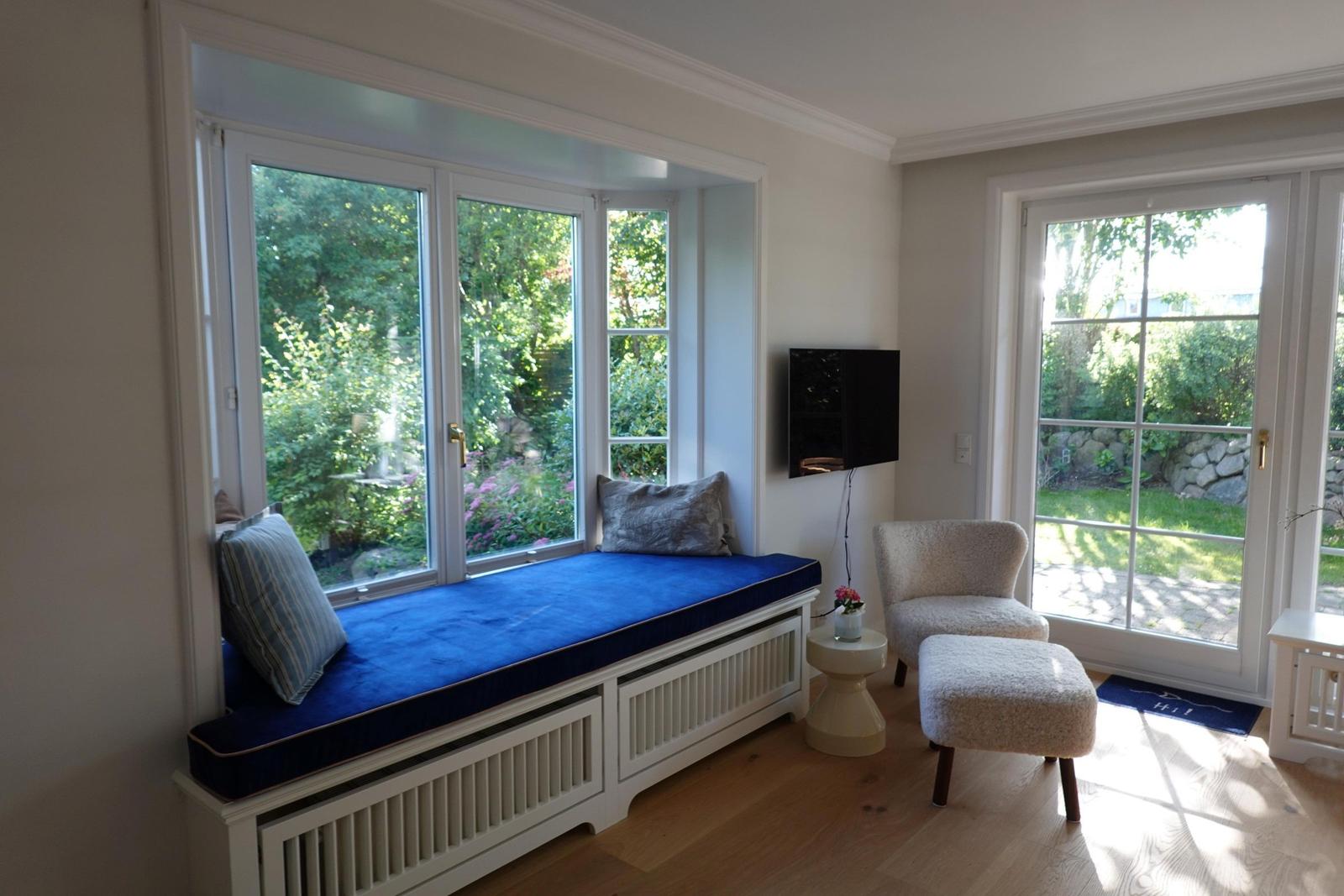 Raum mit Sitzbank vor Fenster, Sessel und Fernseher.