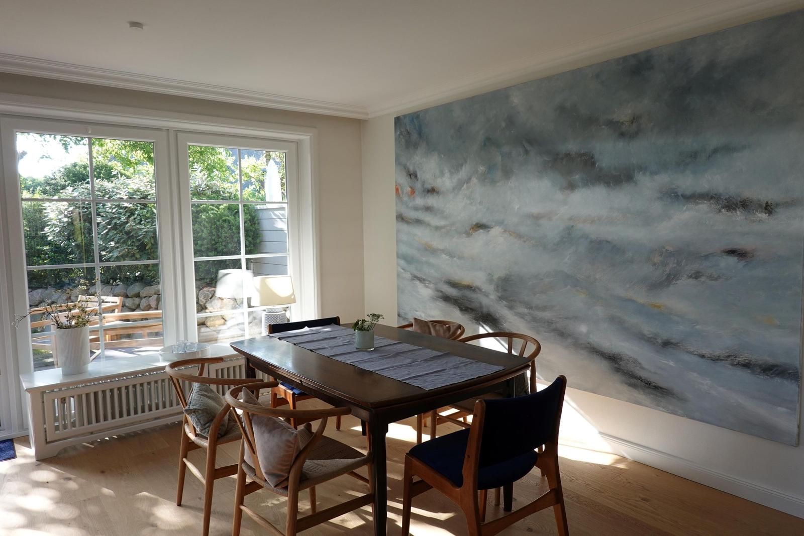 Esszimmer mit Holztisch, Stühlen und großem Wandgemälde. Fenster mit Blick auf Garten.