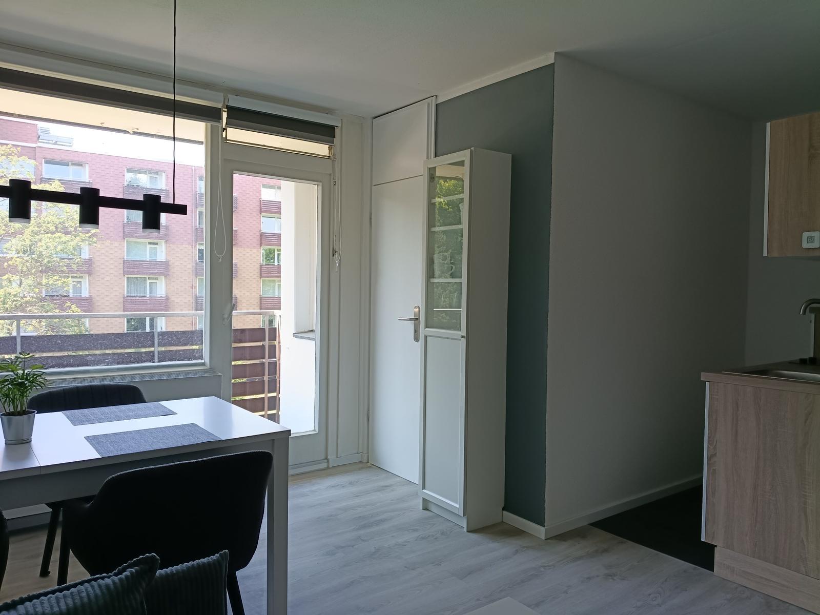 Essbereich mit Tisch, Stühlen und Blick auf Balkon. Küchenzeile und Schrank sichtbar.