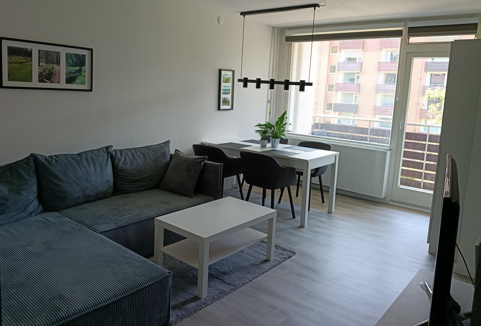 Wohn- und Essbereich mit Sofa, Tisch und Stühlen. Fenster und Balkontür.