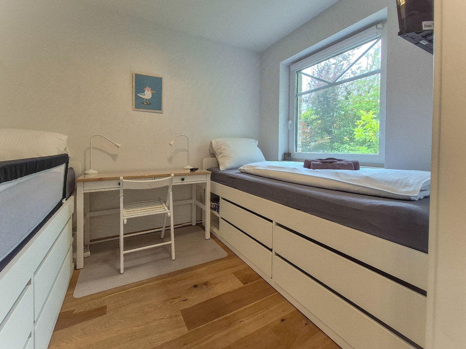 Zimmer mit zwei Betten, Schreibtisch und Fenster mit Blick auf Grün.