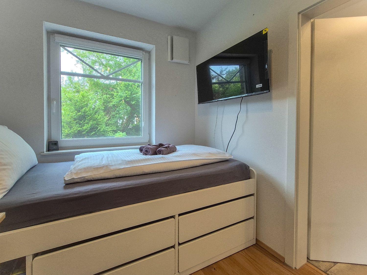 Schlafzimmer mit Bett, TV und Fenster mit Blick auf Bäume.