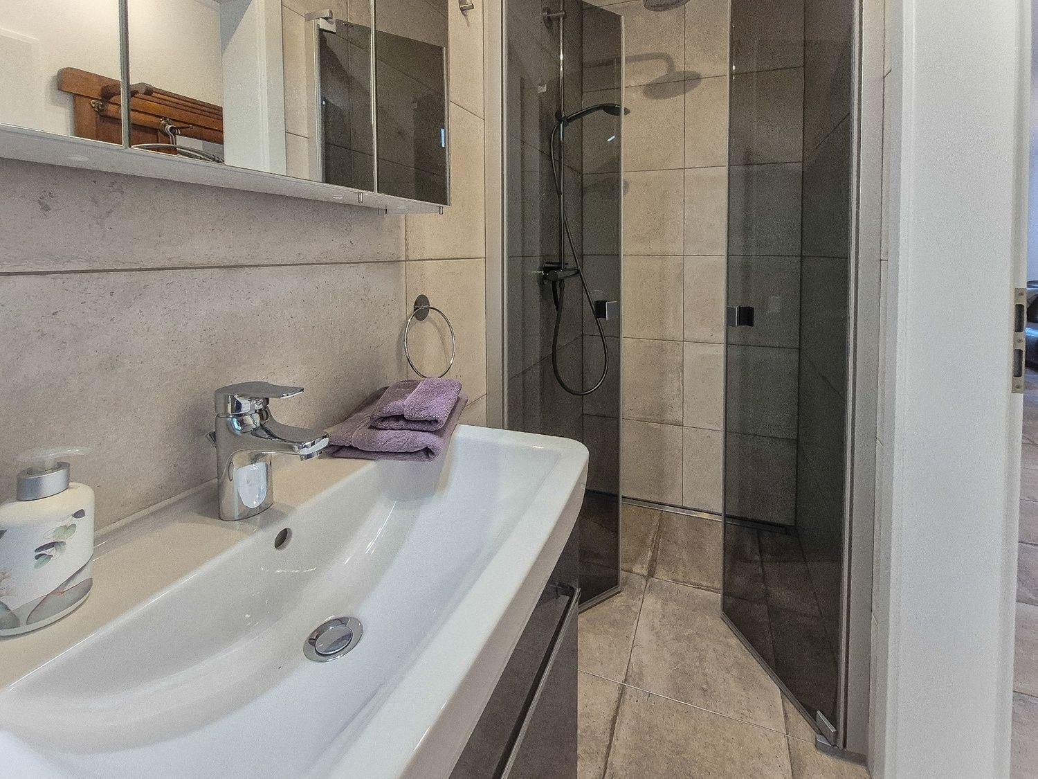 Badezimmer mit Dusche, Waschbecken und Spiegel.