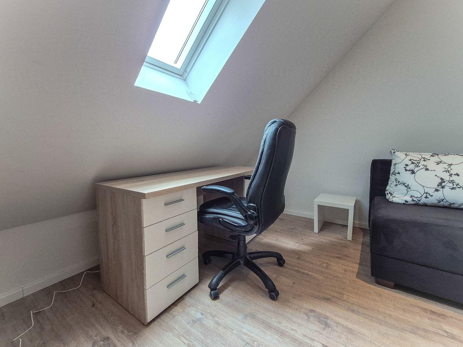 Schreibtisch mit Stuhl unter Dachfenster, Sofa mit Kissen rechts