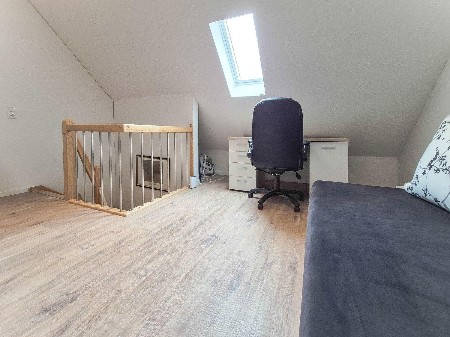 Dachgeschosszimmer mit Schreibtisch, Drehstuhl und Schlafcouch unter Dachschrägen.