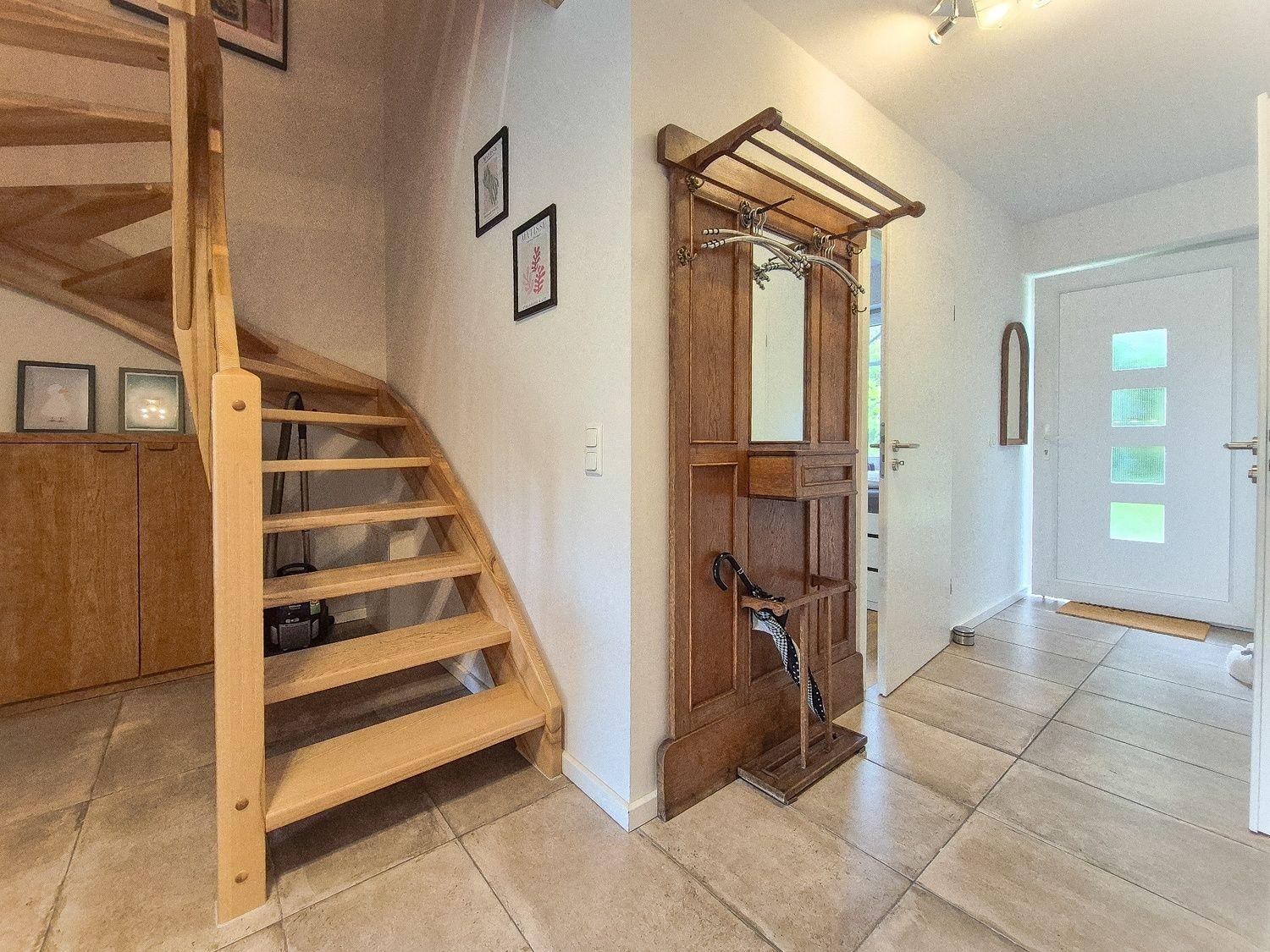 Hausgang mit Holztreppe, Garderobenmöbel und Fliesenboden.