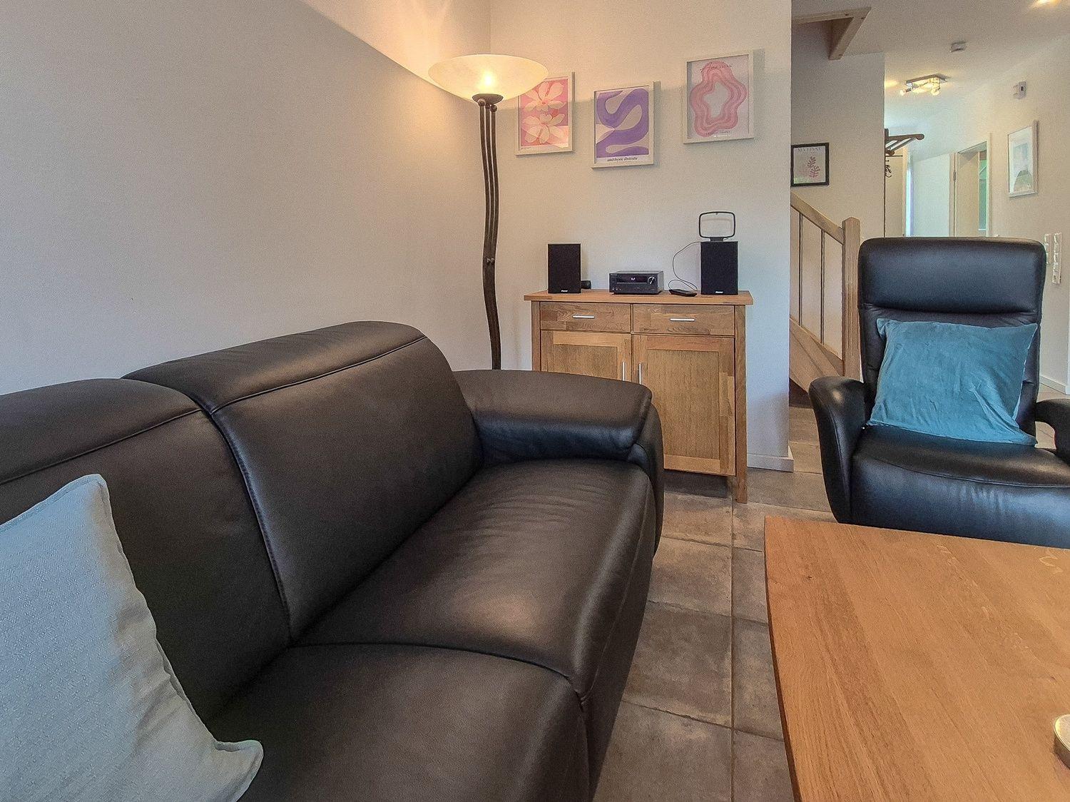Wohnzimmer mit Ledersofa, Sessel, Holztisch und Wandbildern.