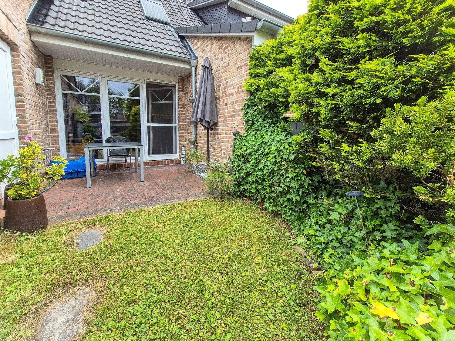 Hinterhof mit Terrasse, Sitzgelegenheit und grüner Hecke.