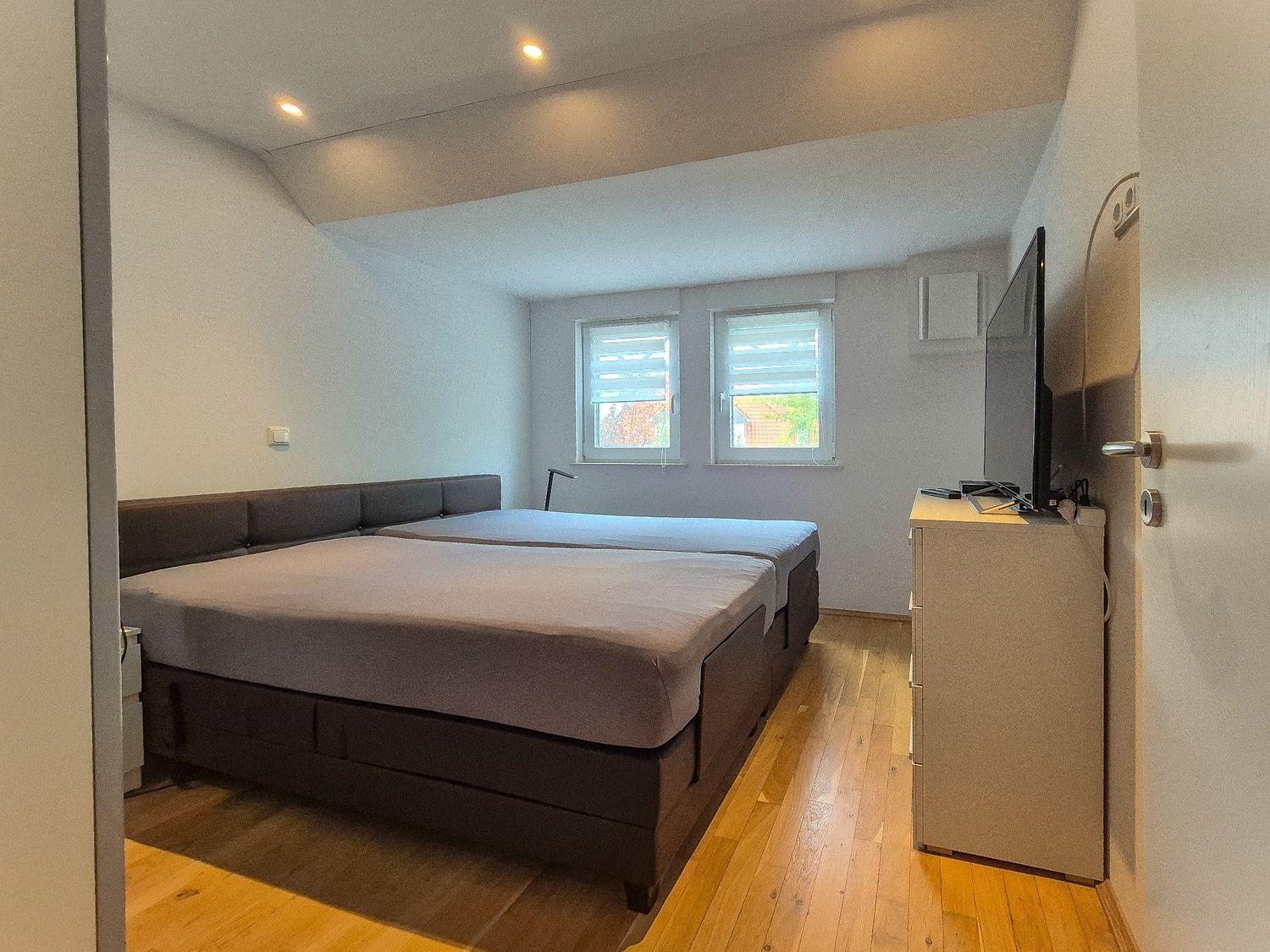 Schlafzimmer mit Doppelbett, zwei Fenstern und TV-Schrank.