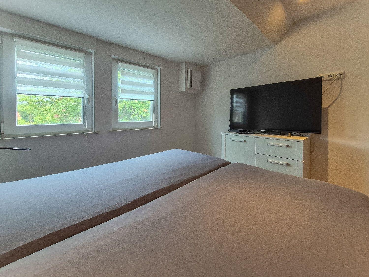 Zwei Betten, Fenster mit Jalousien, TV auf Schrank