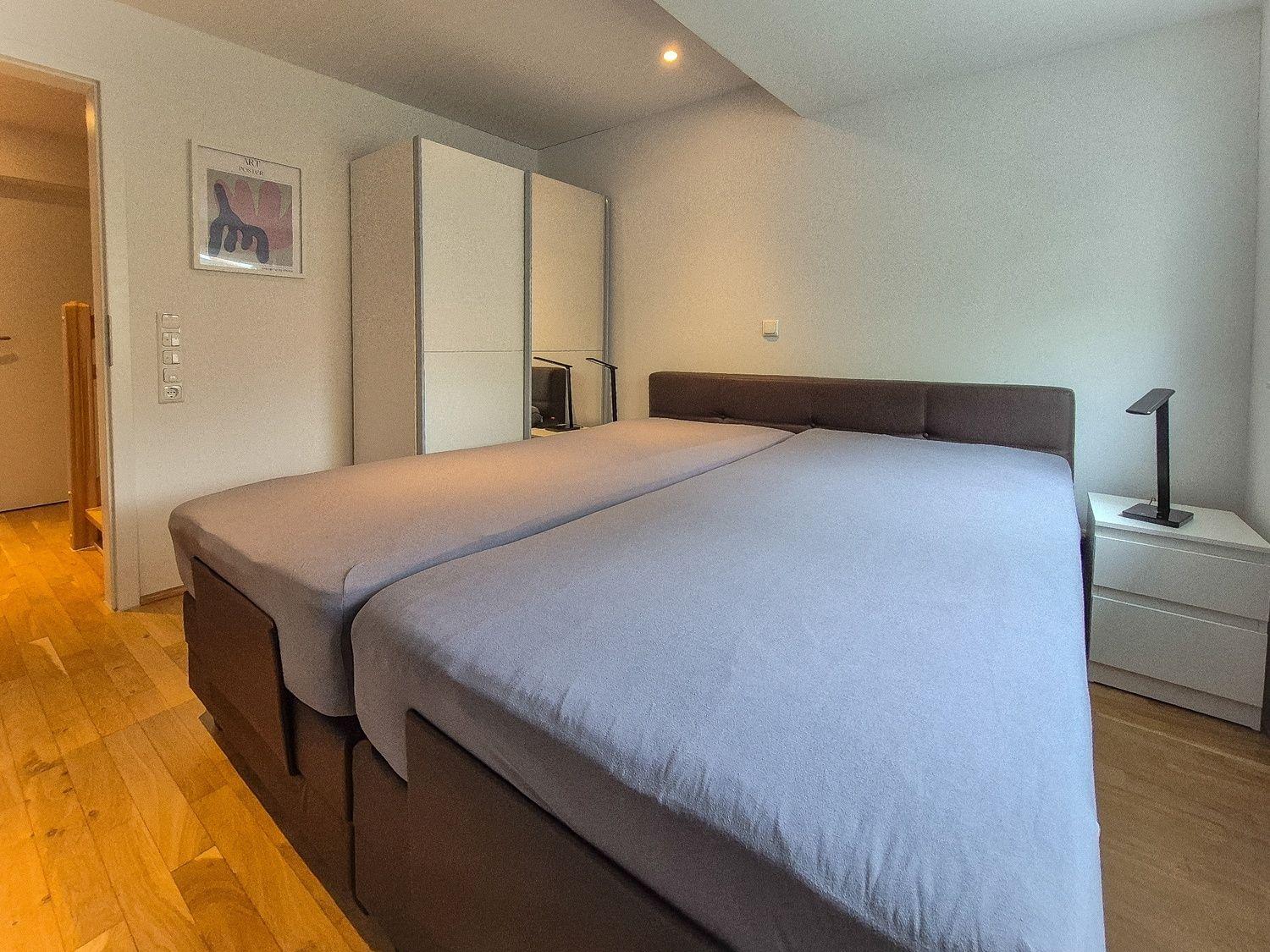 Doppelbett mit grauer Bettwäsche, Nachttisch und Kleiderschrank im Schlafzimmer.