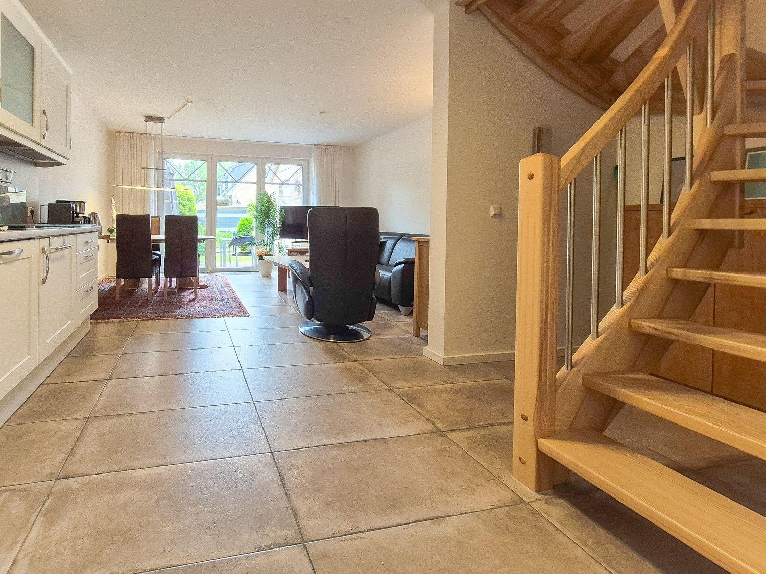 Haus mit Küche, Essbereich und Wohnzimmer. Holztreppe führt nach oben.