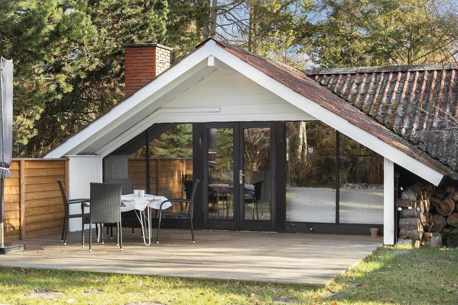 Terrasse mit Tisch und Stühlen vor einem Haus mit Glasfront und Schornstein.