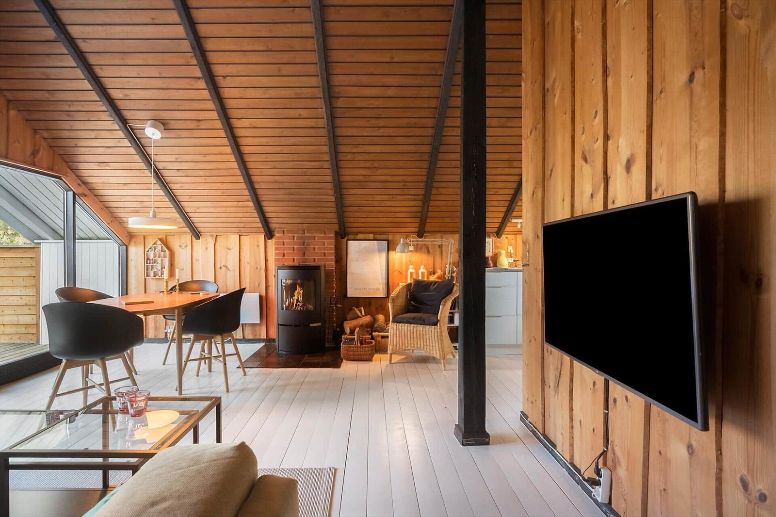 Wohnraum mit Holzwand, Kamin und TV. Essbereich mit Tisch und Stühlen.