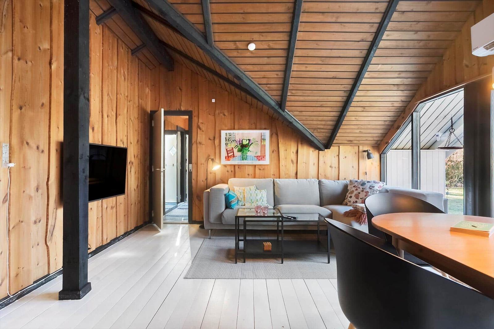 Wohnraum mit Holzwand, Sofa, Tisch und TV. Dachbodenstruktur mit Holzdecke.