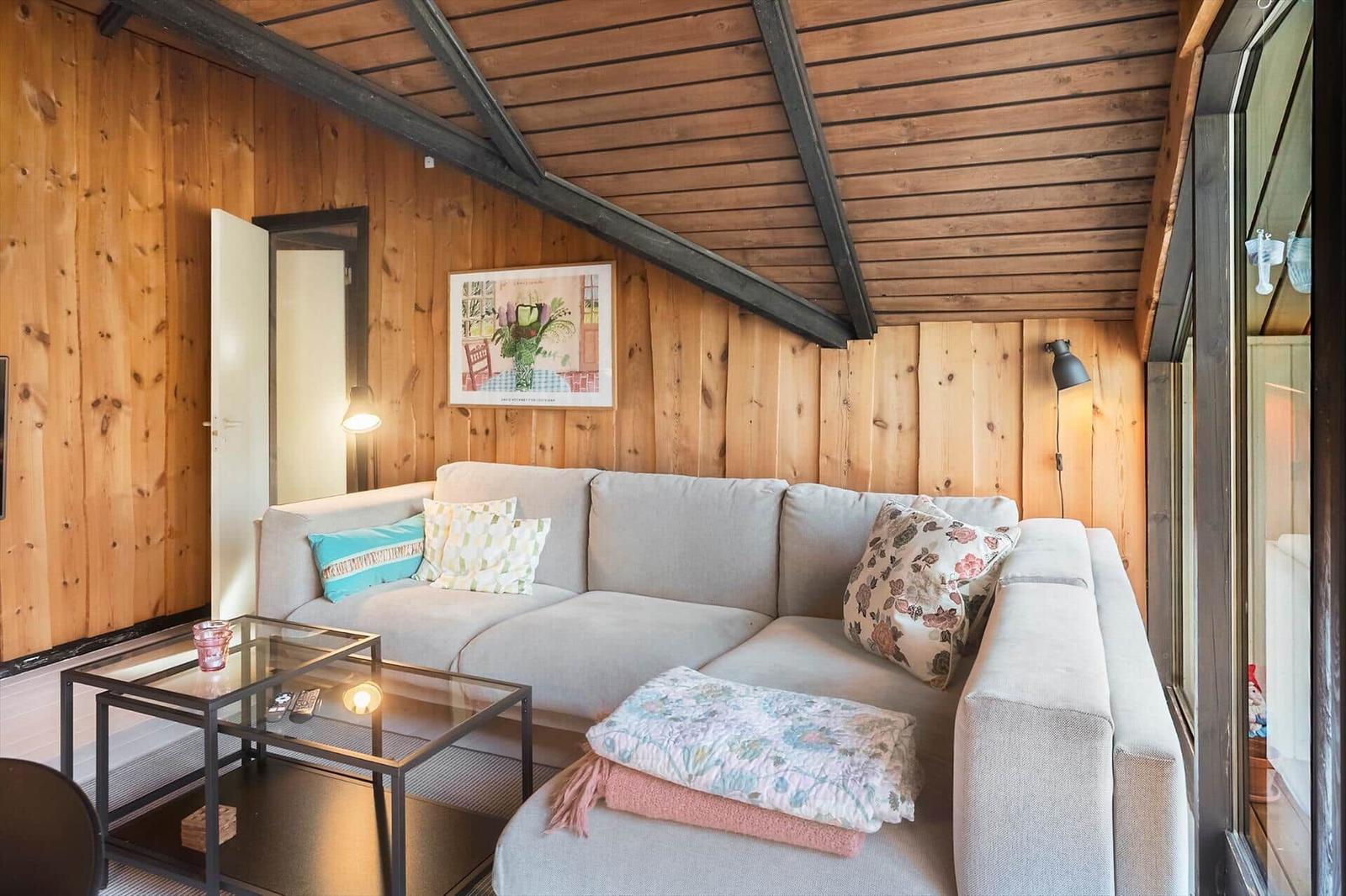 Wohnzimmer mit Sofa, Couchtisch und Holzwand. Deckenbalken und Fenster sichtbar.