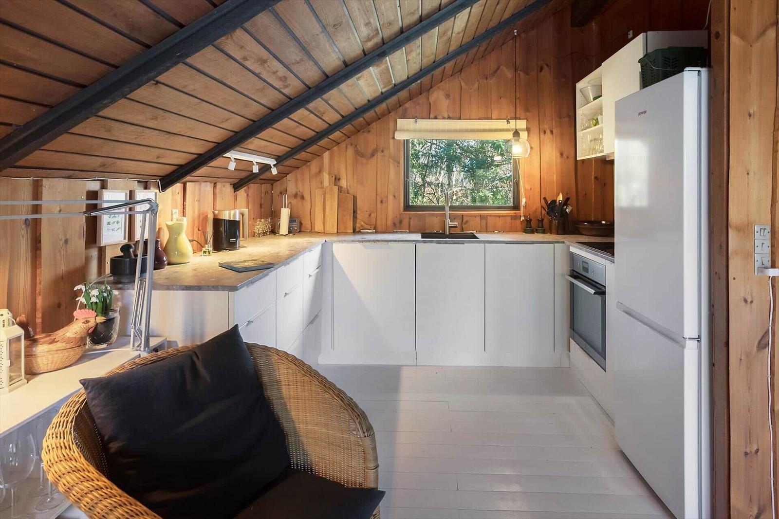 Küche mit weißen Schränken, Kühlschrank und Arbeitsfläche unter Holzdecke.