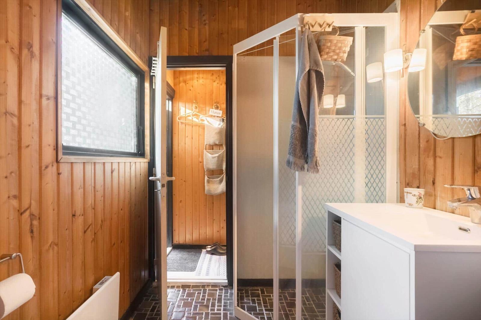 Badezimmer mit Dusche, Waschbecken und Holzwandverkleidung.