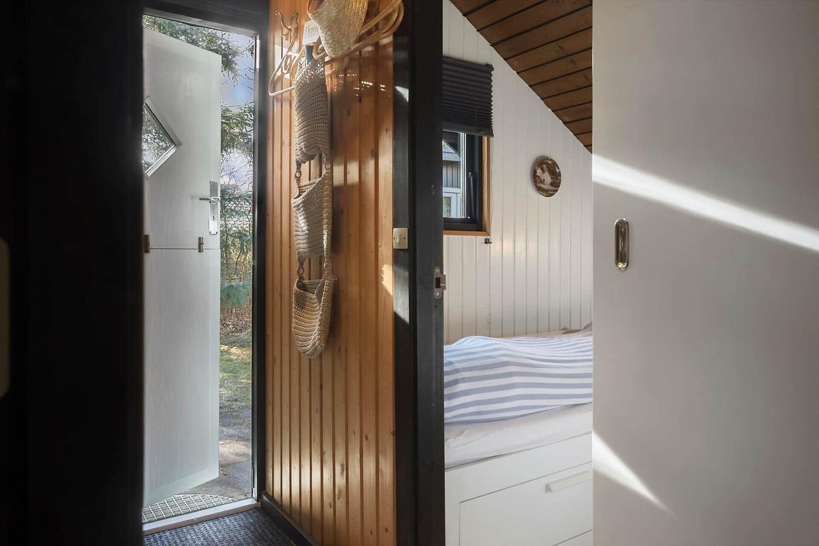 Schlafzimmer mit Bett und Holzwand. Tür führt nach draußen.