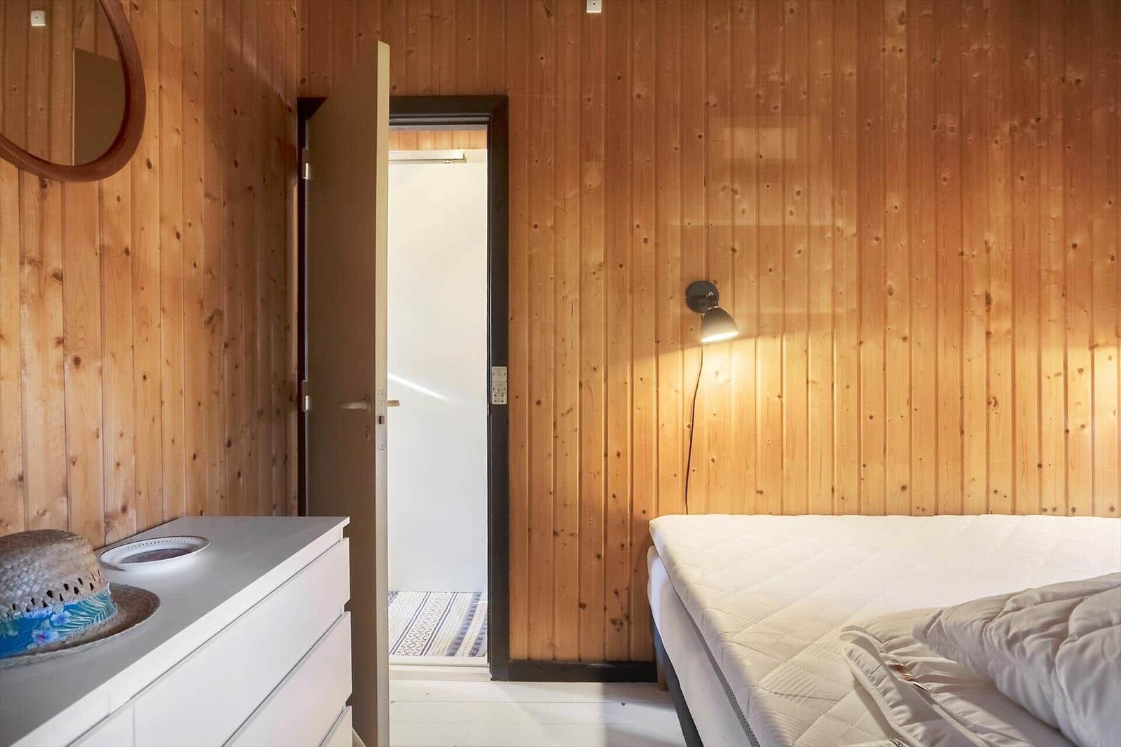 Schlafzimmer mit Holzwand, Bett, Nachttisch und Tür zum Bad.