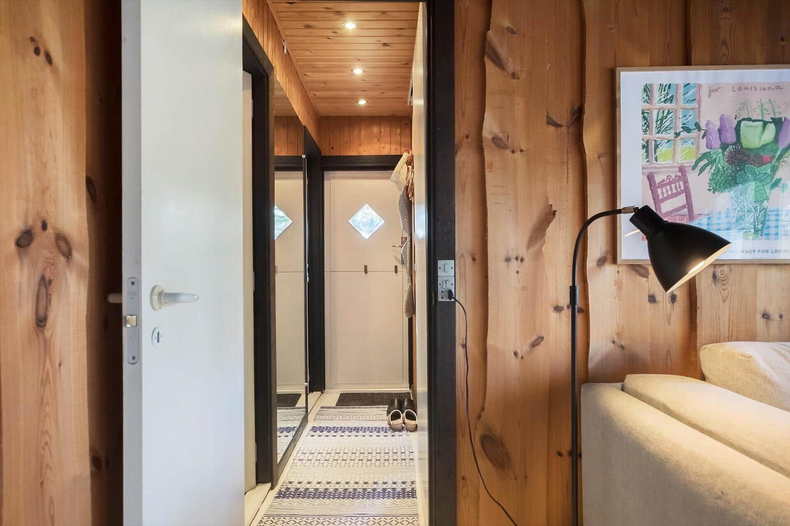 Holzgetäfelte Türöffnung zeigt Flur mit Teppich und Schlafzimmer mit Stehlampe.