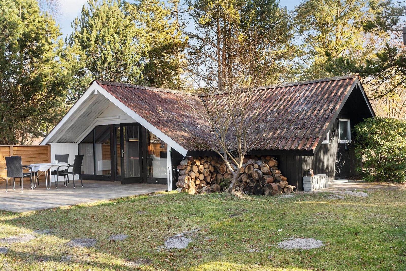 Haus mit Terrasse, Tisch, Stühlen und Holzstapel unter Dach