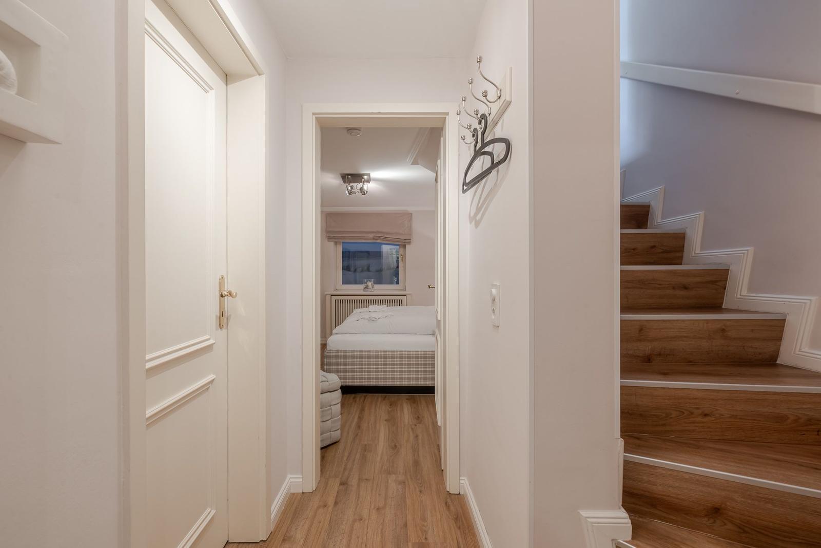Flur mit Schlafzimmer und Treppe. Holzboden, weiße Wände, Bett mit Kissen.