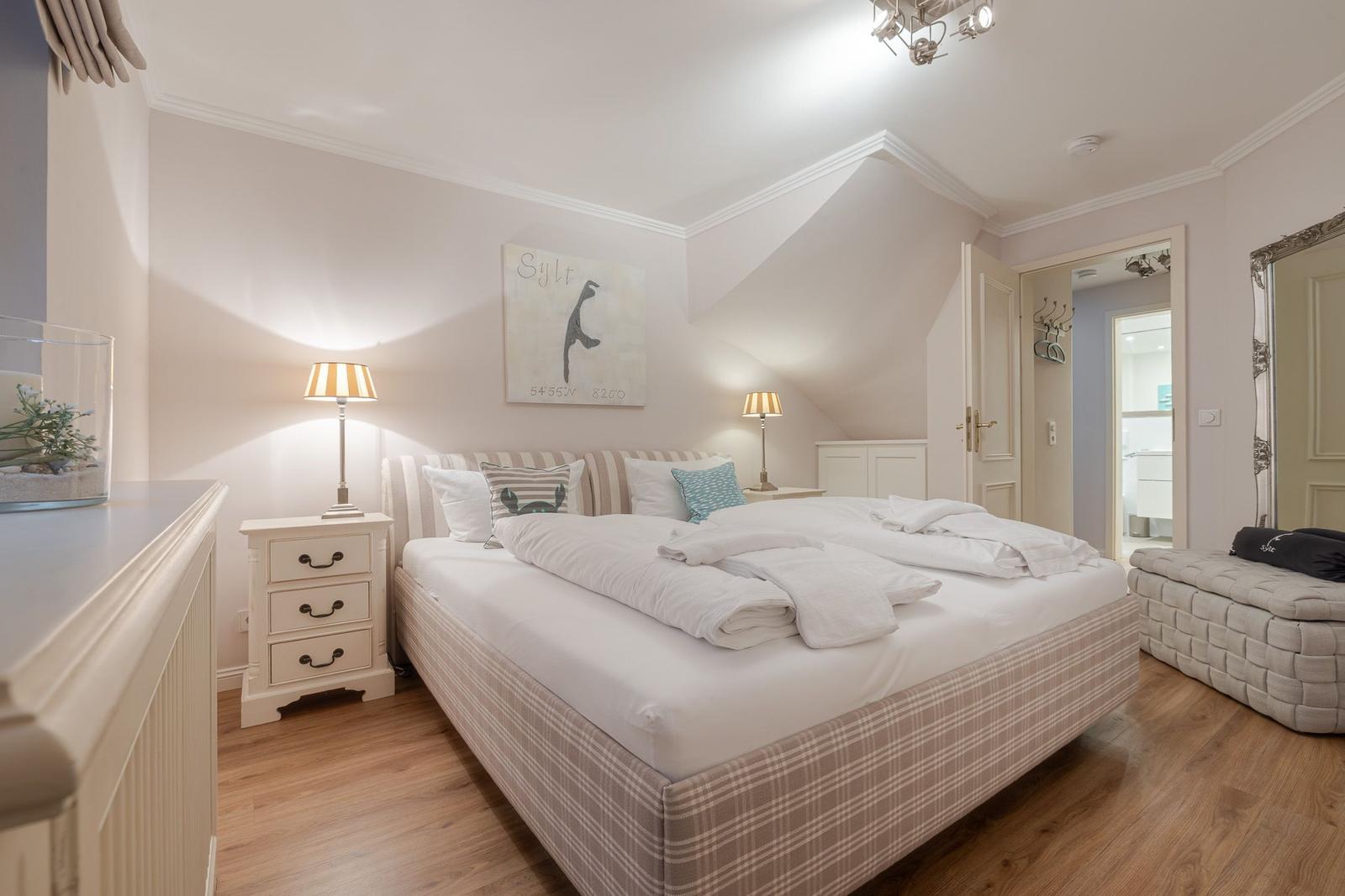 Schlafzimmer mit Doppelbett, Nachttischen und Wandbild. Holzboden und Einbaukabinett sichtbar.