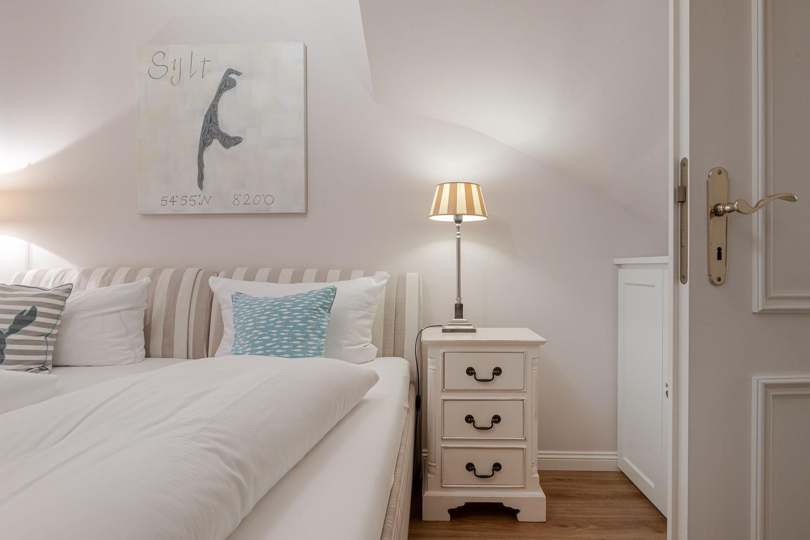 Schlafzimmer mit Bett, Nachttisch und Wandbild. Dachgeschoss mit schräger Decke.