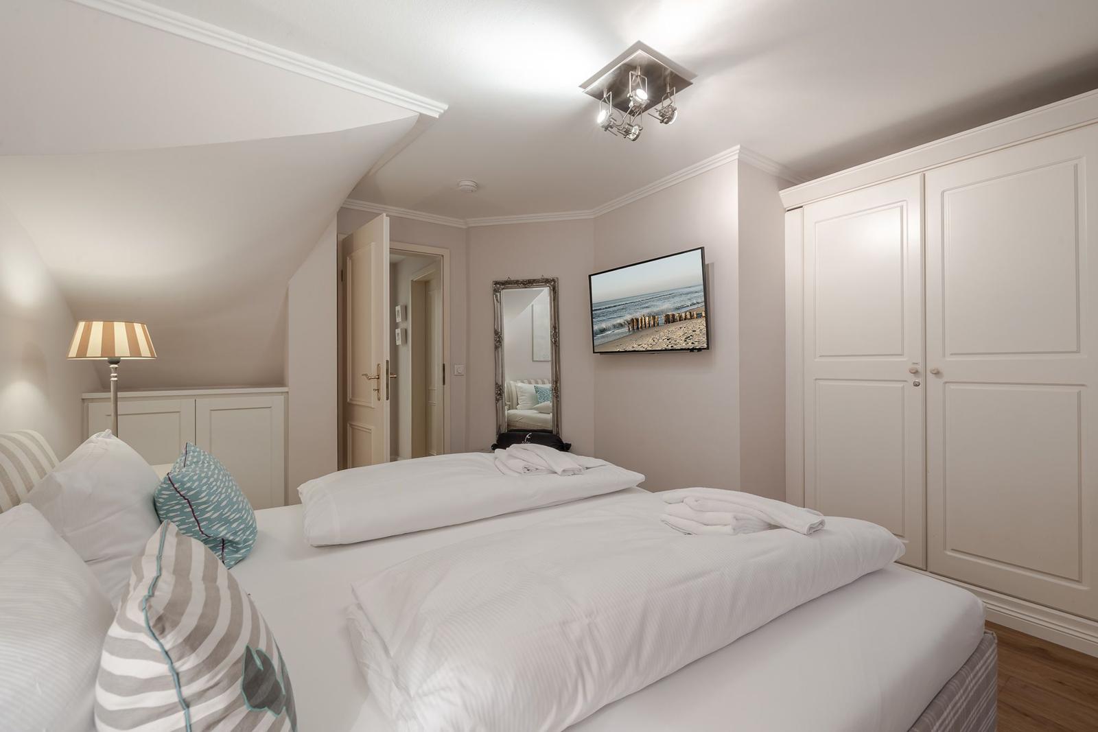 Schlafzimmer mit Doppelbett, Kleiderschrank und Fernseher an der Wand.