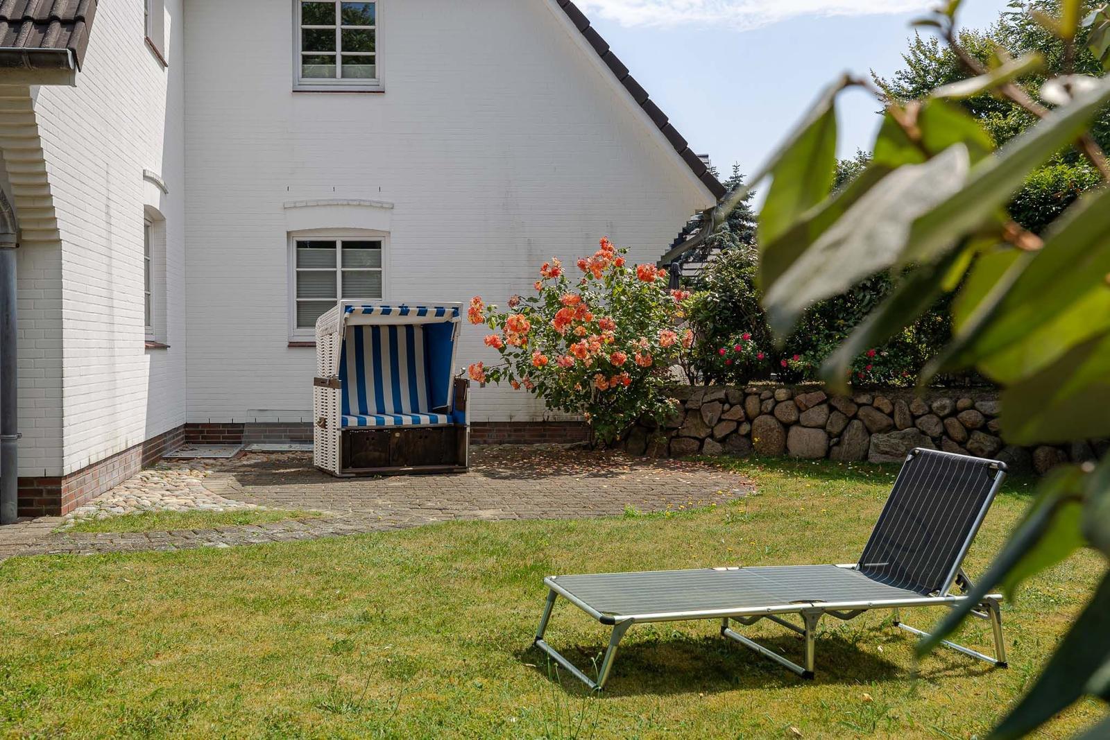 Hinterhof mit Strandkorb, Liegestuhl und blühenden Rosen.