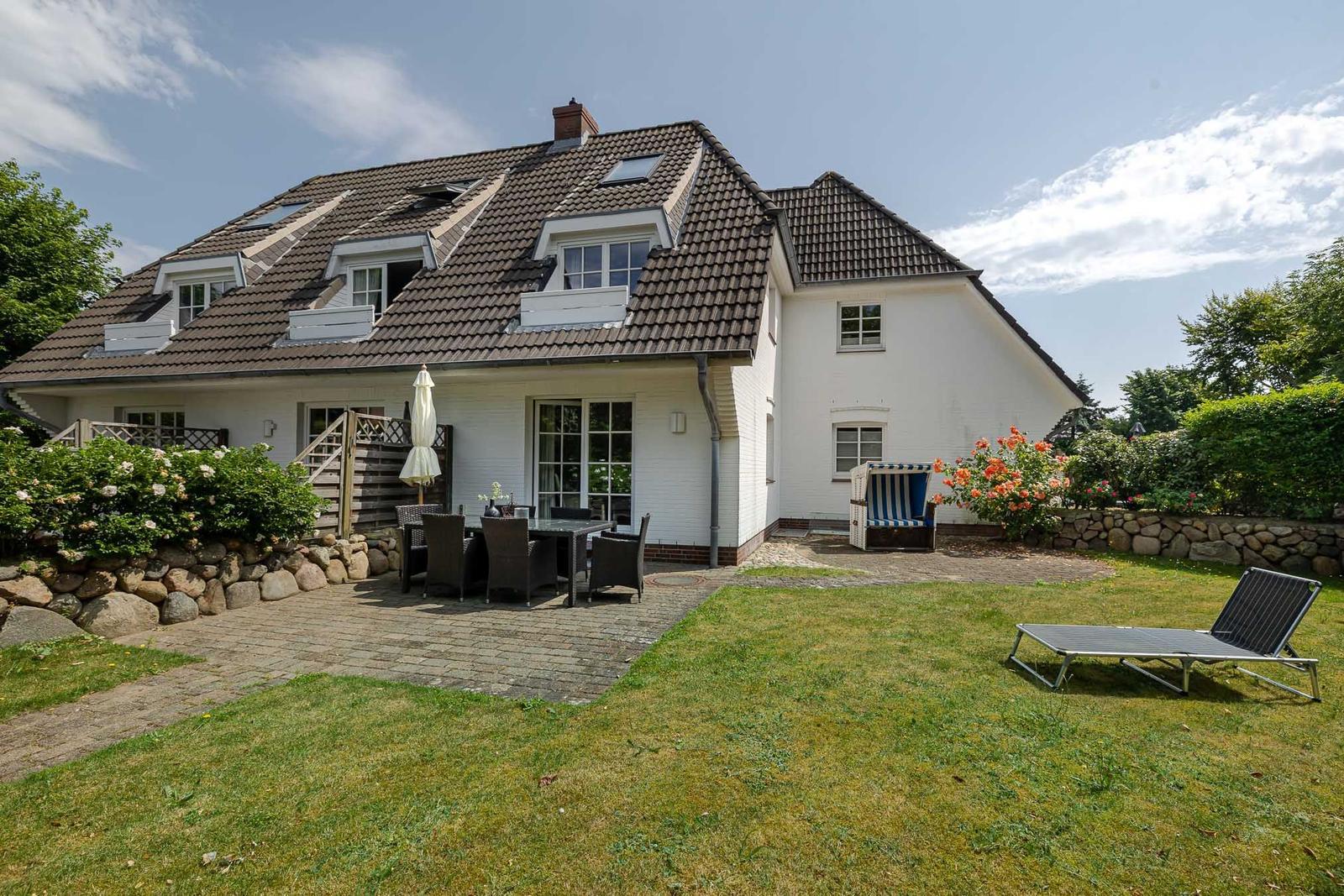 Wohnhaus mit Terrasse, Garten und Liegestuhl. Holzveranda und Blumenbeete.