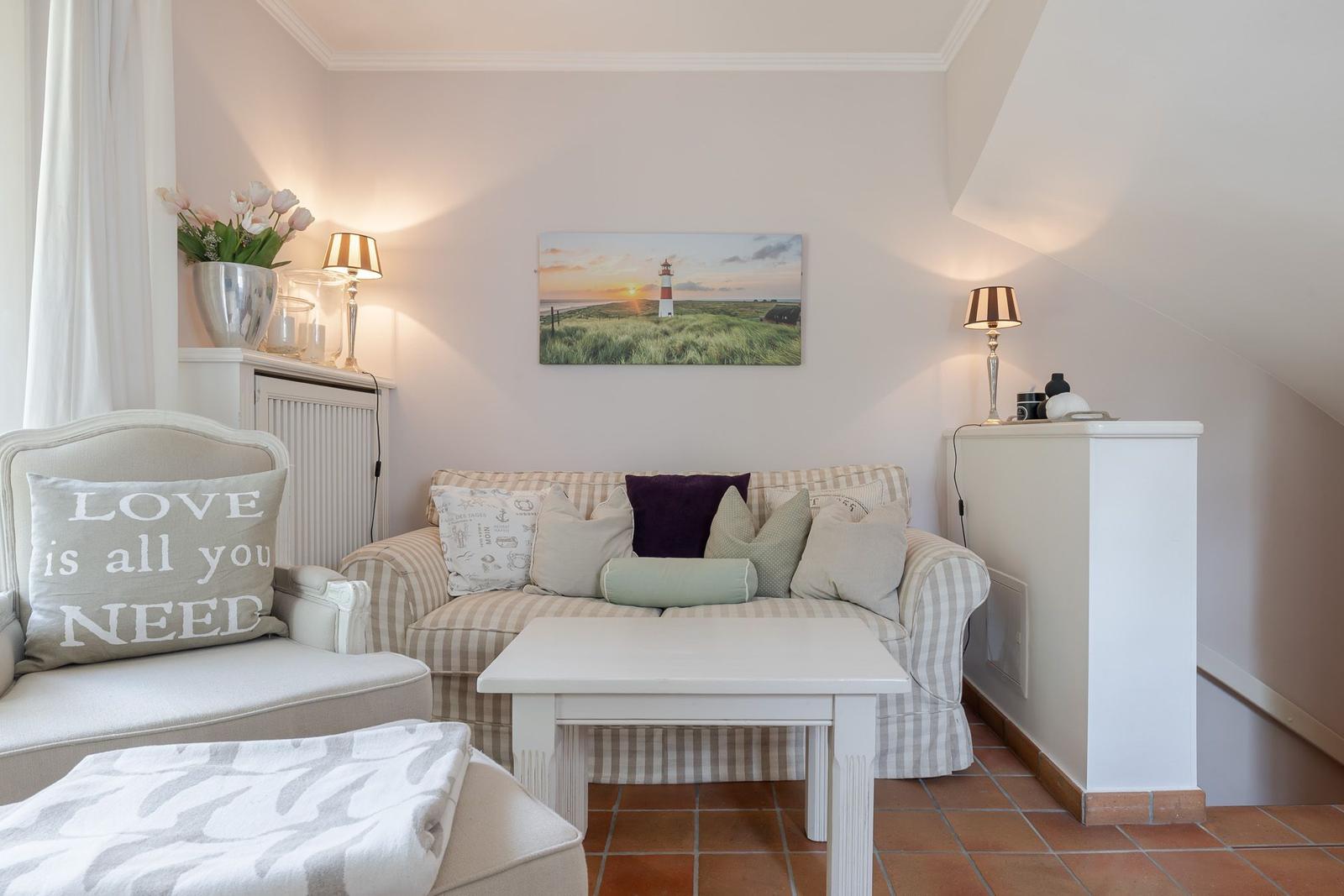 Wohnzimmer mit Sofa, Sessel und Tisch unter schräger Decke.