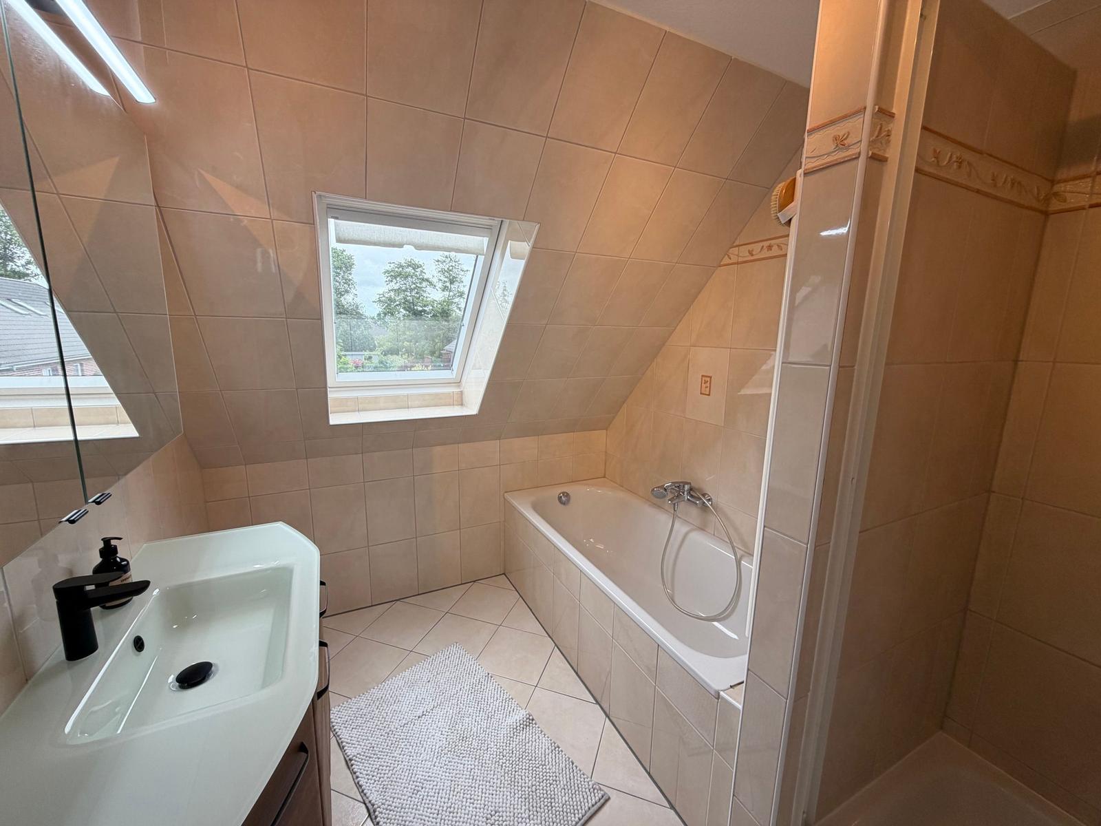 Badezimmer mit Badewanne, Dusche und Fenster mit Blick auf Garten.