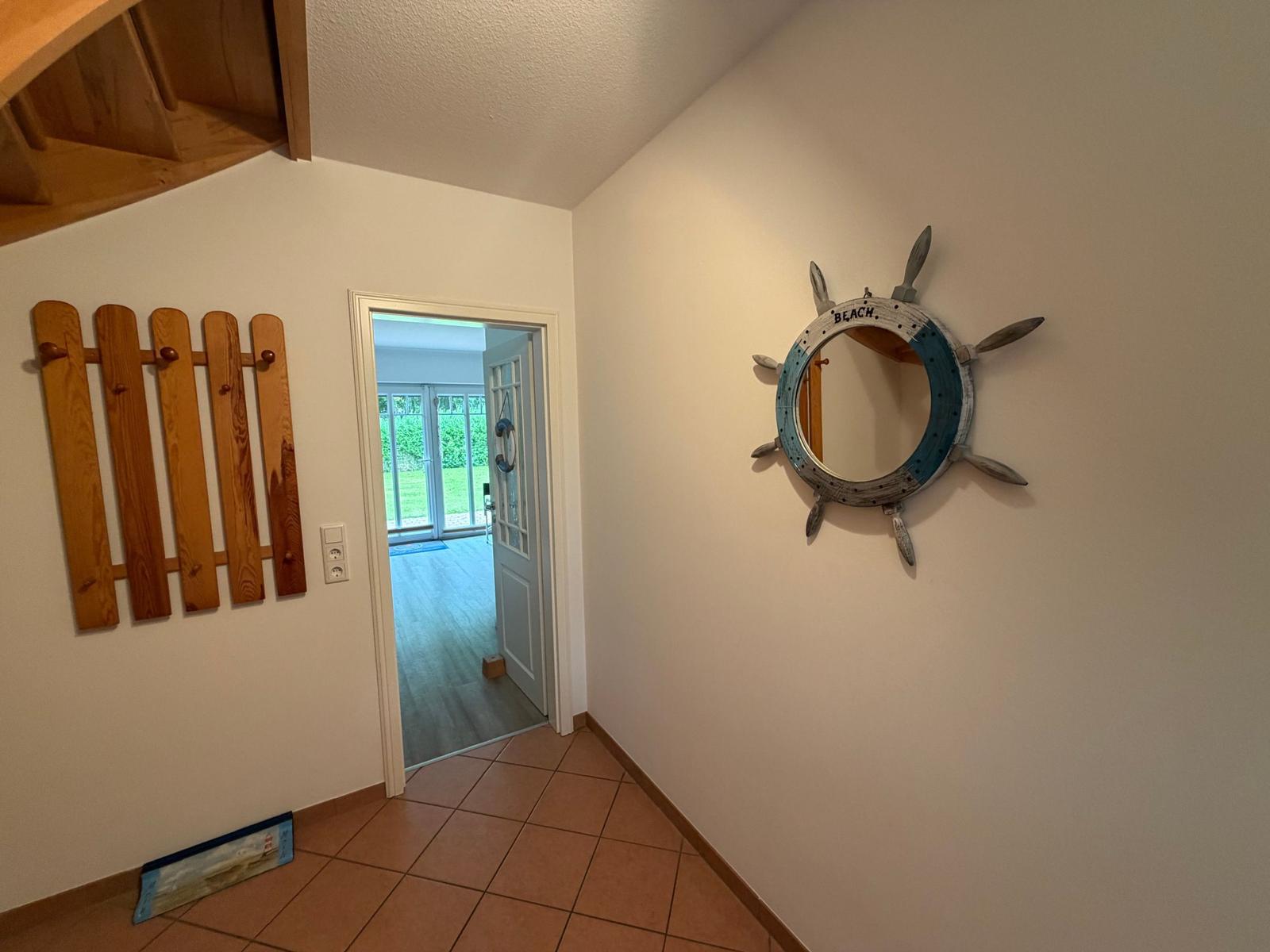 Eingangsbereich mit Holzdekor und runden Spiegel mit Ruderhausmotiv an der Wand.
