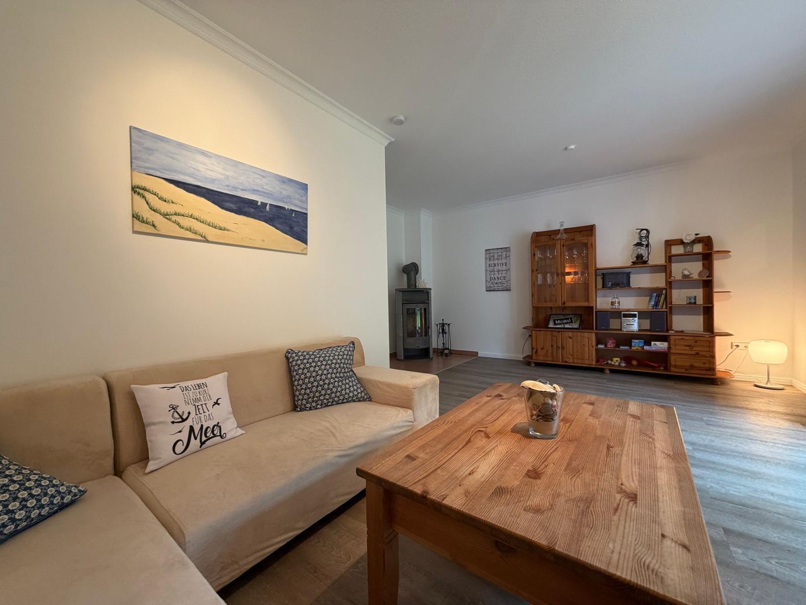 Wohnzimmer mit Sofa, Holztisch und Wandbild. Im Hintergrund steht ein Kamin und ein Bücherregal.
