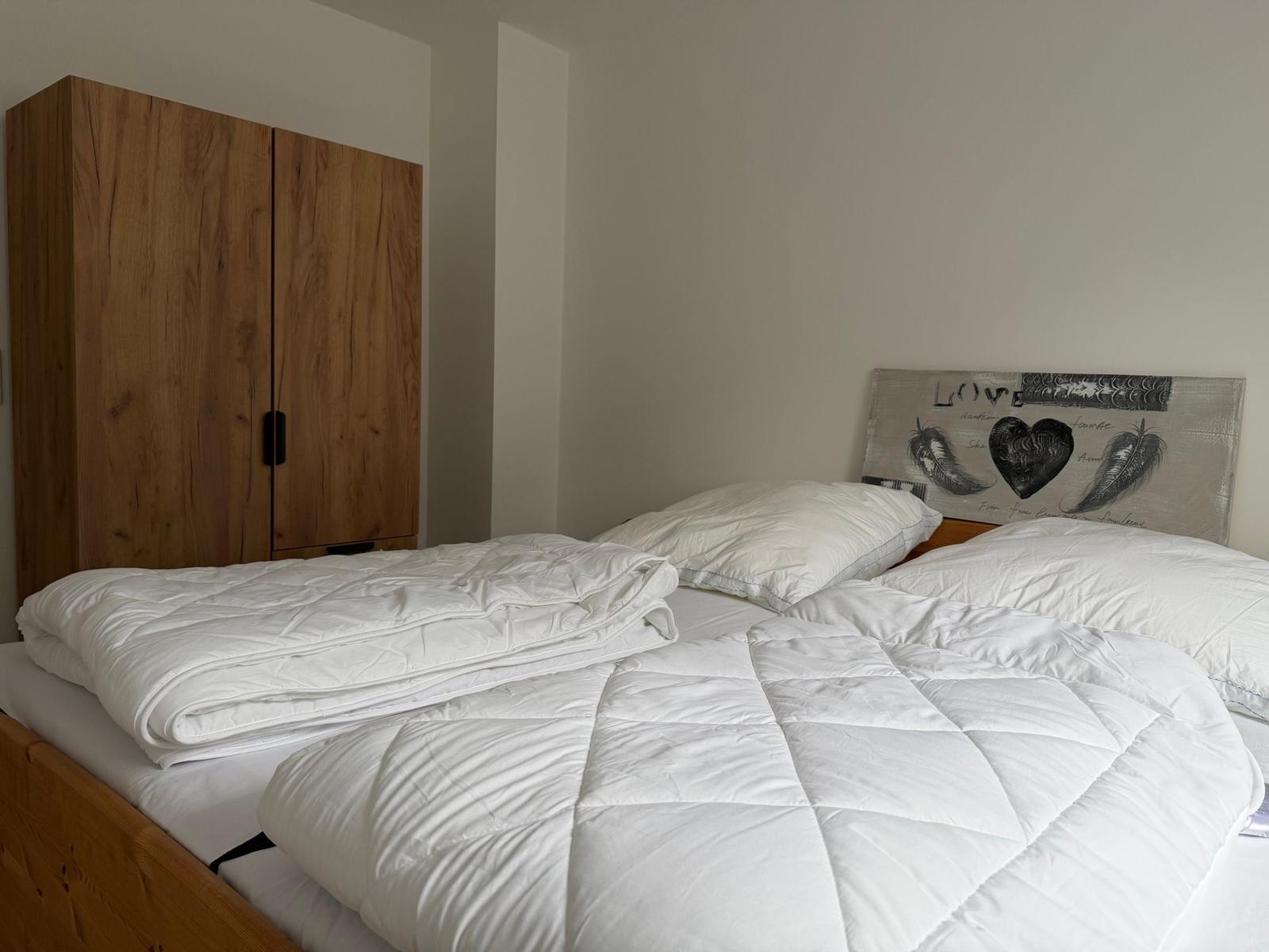 Schlafzimmer mit Bett, weißer Bettwäsche und Holzschrank.