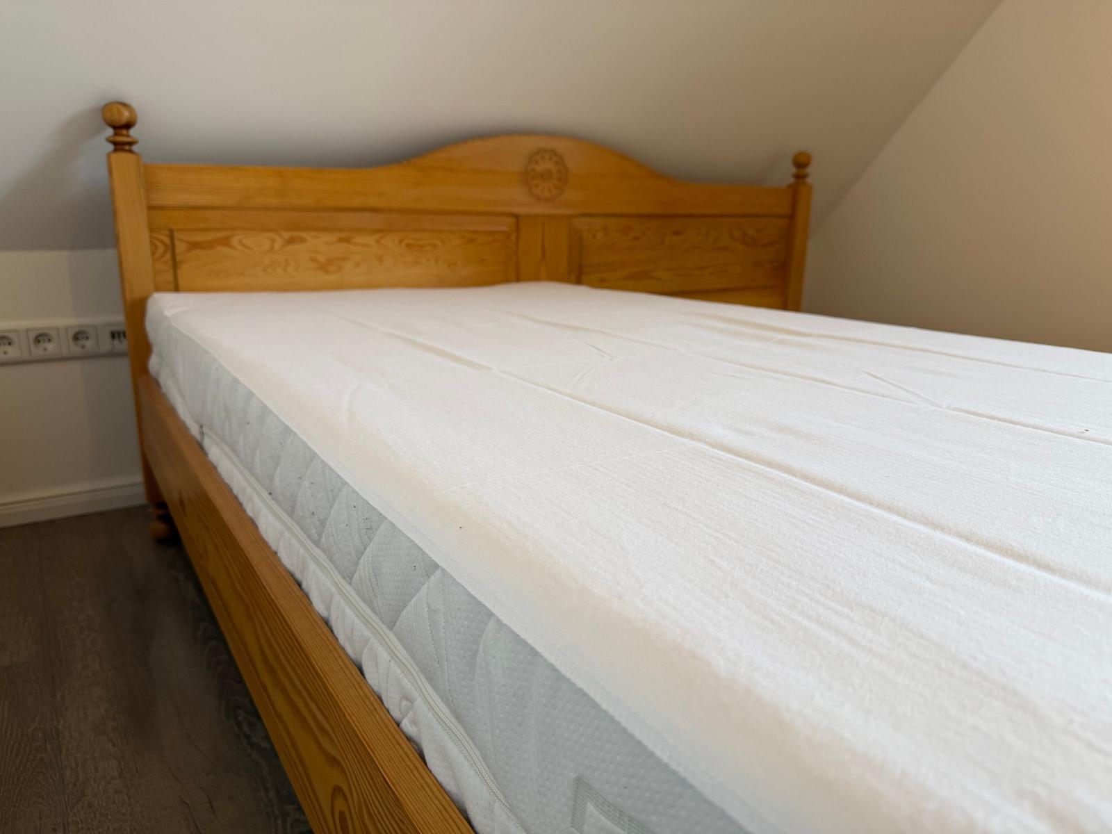Hölzernes Bett mit weißer Matratze in einem Raum mit geneigtem Dach.