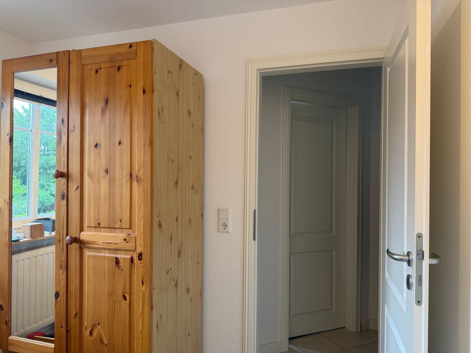 Holzschrank mit Spiegeltür, Türöffnung und Steckdose an Wand