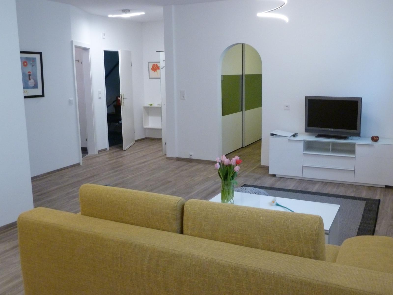 Wohnzimmer mit gelbem Sofa, Fernseher und Holzboden.