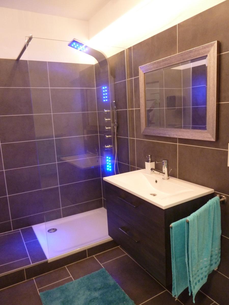 Dusche mit LED-Beleuchtung, Waschbecken und Spiegel an der Wand.